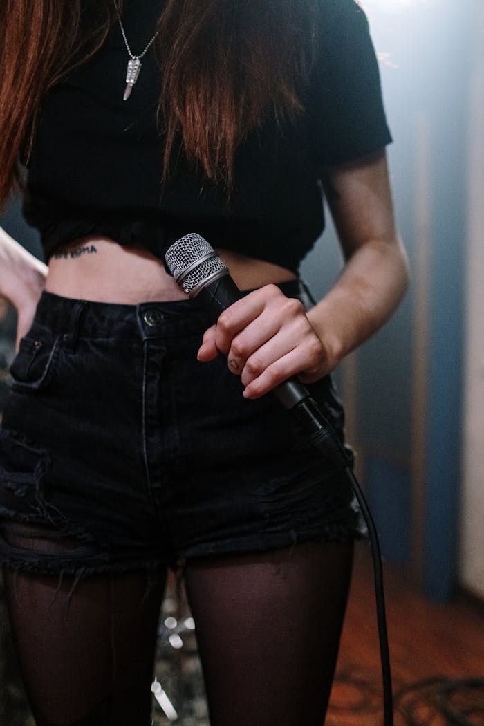 Young woman singer holding a microphone on stage in edgy attire, ready to perform.